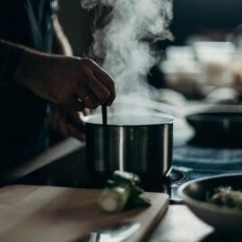 Persona cocinando en una cocina con vapor que sale de una olla en el fogón.