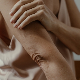 Primer plano de una mujer con chaleco con el brazo cruzando el pecho sujetándose el otro brazo.
